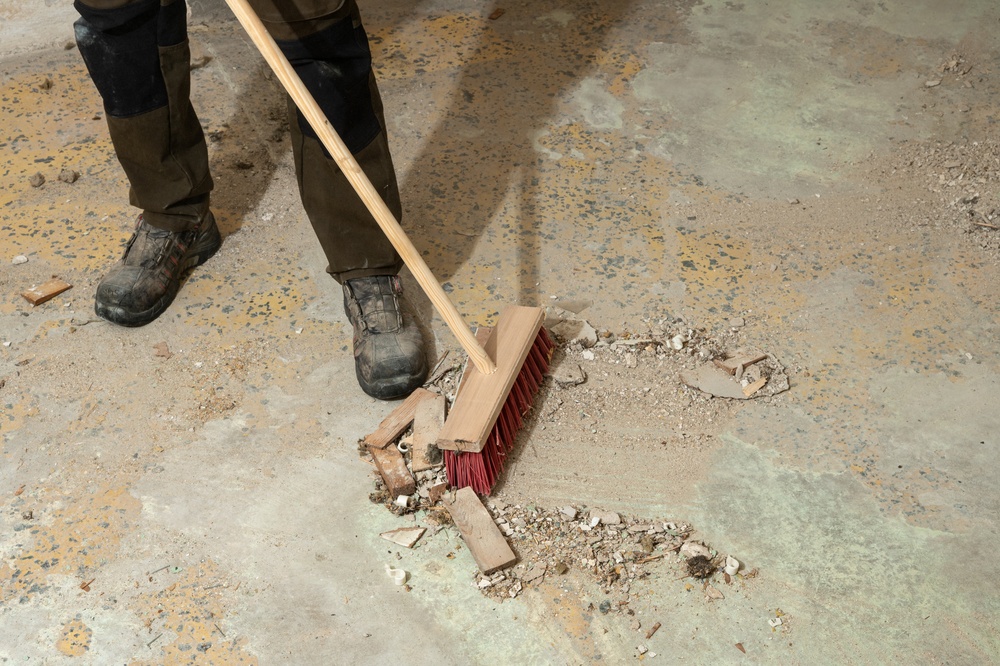 Worker in heavy boots sweeping construction debris from a concrete floor