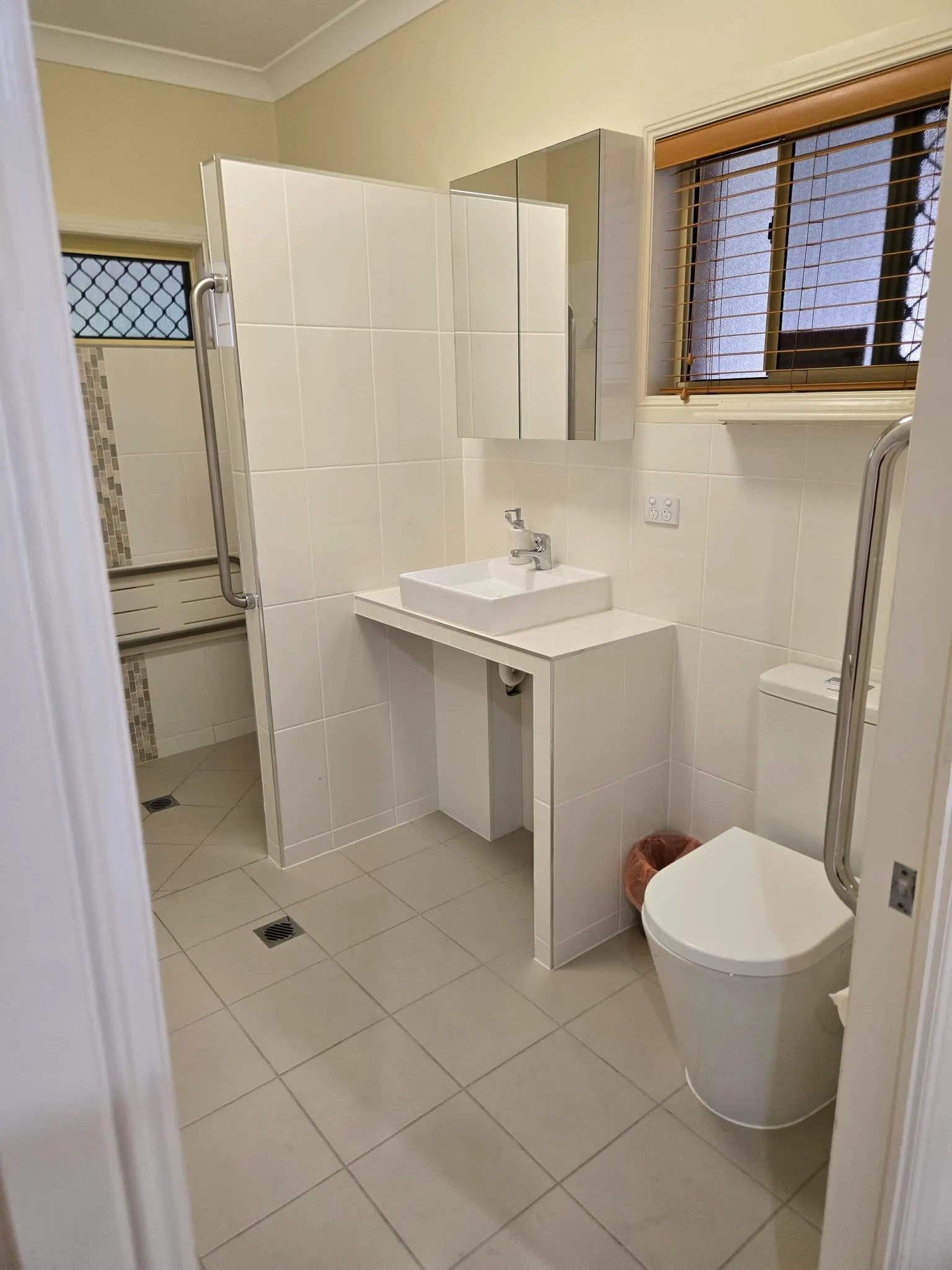 White-tiled bathroom with vessel basin, toilet and grab rails