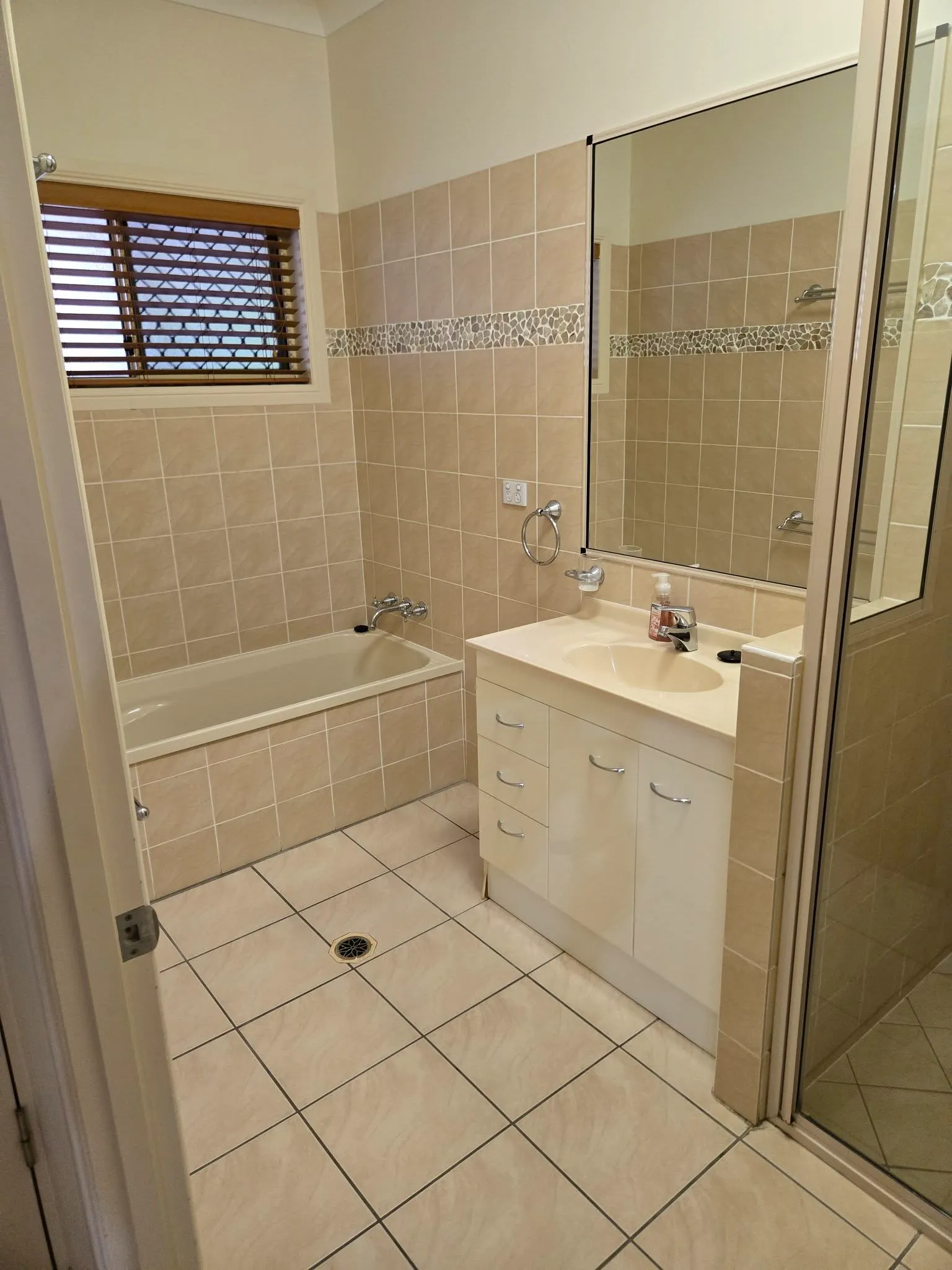 Beige-tiled bathroom with built-in bathtub, vanity and shower screen