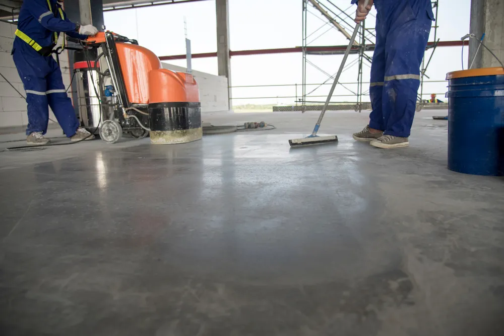 Two workers polishing a concrete slab with a floor grinder and squeegee