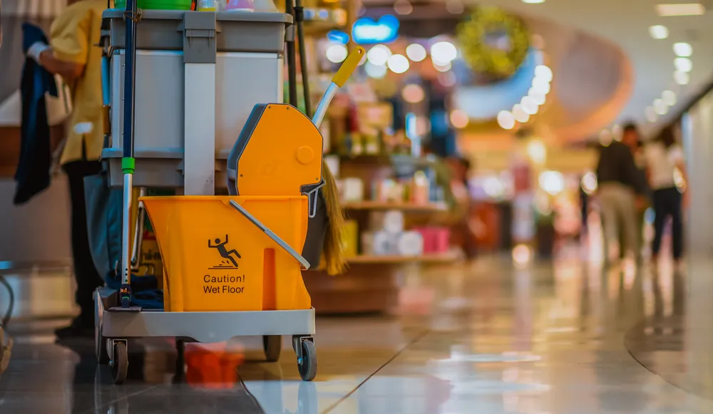 Yellow mop bucket on a cleaning trolley on a polished tile floor