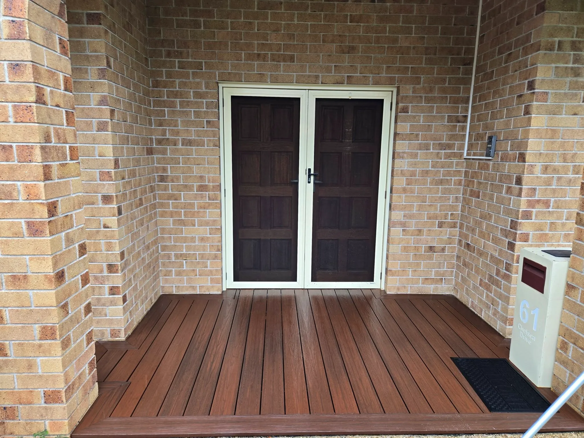 Freshly cleaned brick entryway with stained timber double doors and decking at a Townsville home